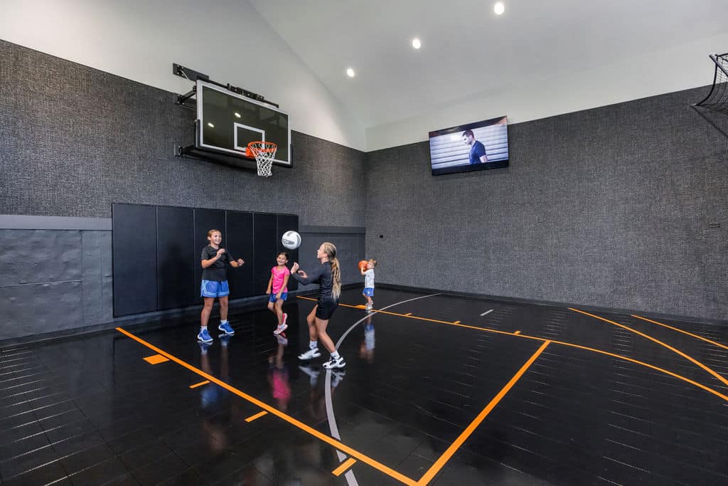 Nicholas Design Build | Four people playing basketball in an indoor court with a hoop and black flooring. A screen displays a video on the wall.