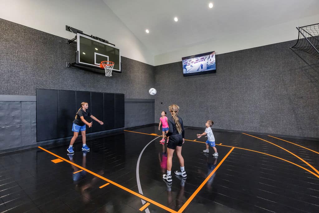 Nicholas Design Build | Four people play basketball in an indoor court. One person prepares to pass the ball, while others observe. A TV is mounted on the wall.