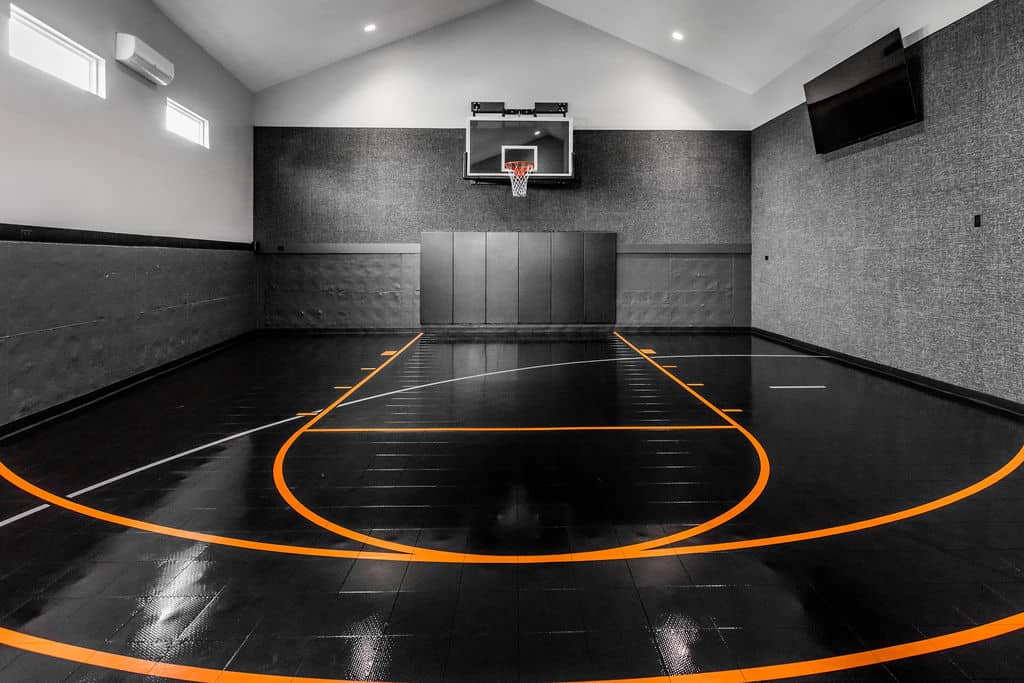 Nicholas Design Build | Indoor basketball court with a black and orange design, featuring a hoop, polished floor, and high walls.