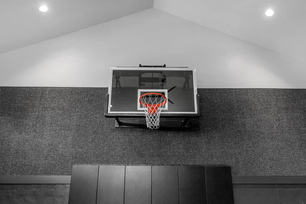 Nicholas Design Build | A basketball hoop with a clear backboard is mounted on a textured wall inside a building.