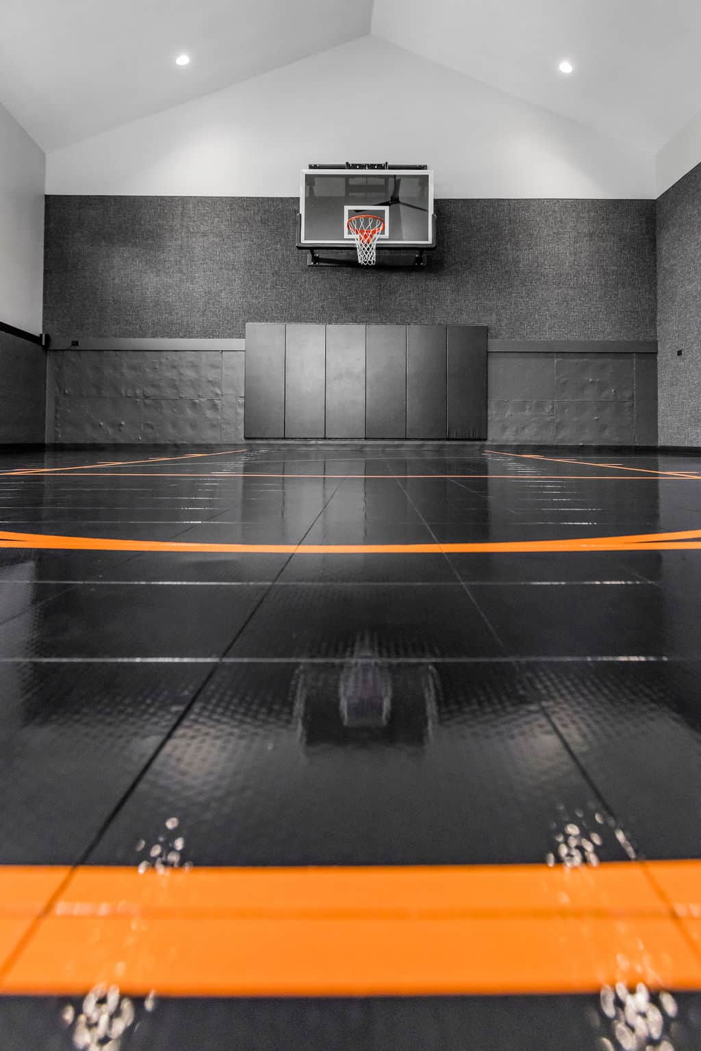 Nicholas Design Build | Indoor sports court with black flooring and orange lines, featuring a basketball hoop mounted on the wall.