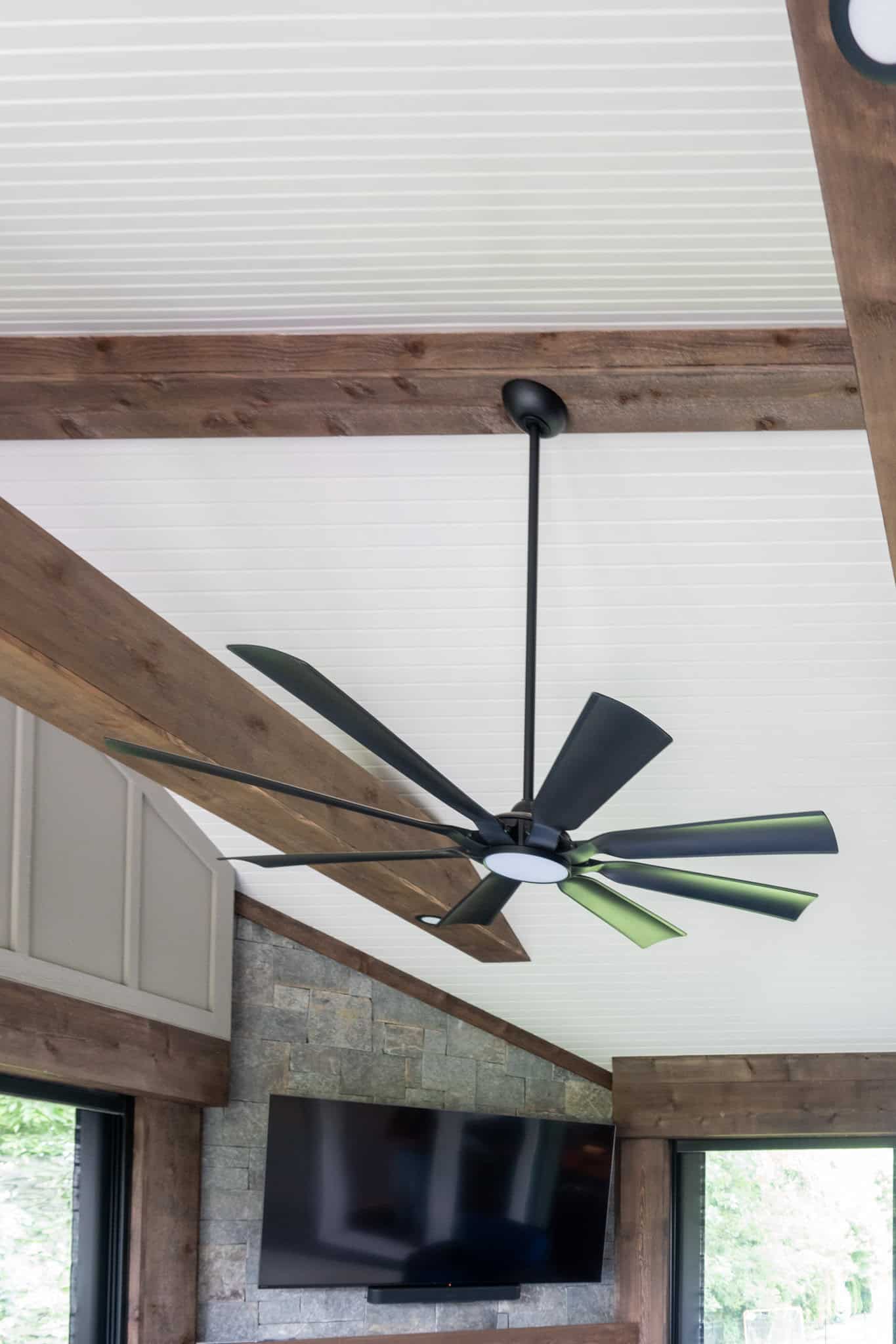 Nicholas Design Build | Ceiling with wooden beams and a large black ceiling fan. Below is a wall-mounted flat-screen TV.