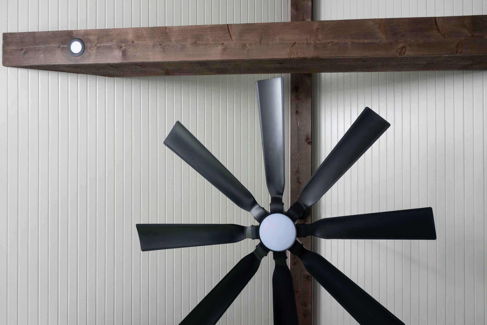 Nicholas Design Build | Ceiling fan with eight black blades mounted on a wooden beam against a white paneled ceiling.