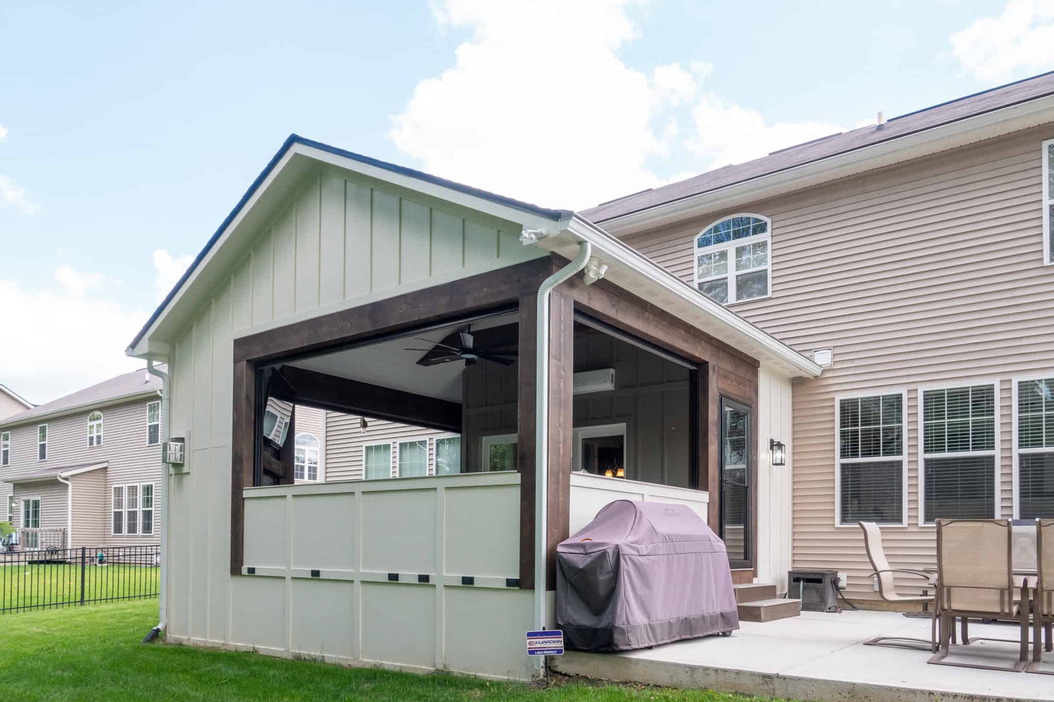 Nicholas Design Build | A residential back porch with a grill, outdoor seating, and a ceiling fan, partially enclosed by screens, attached to a house.