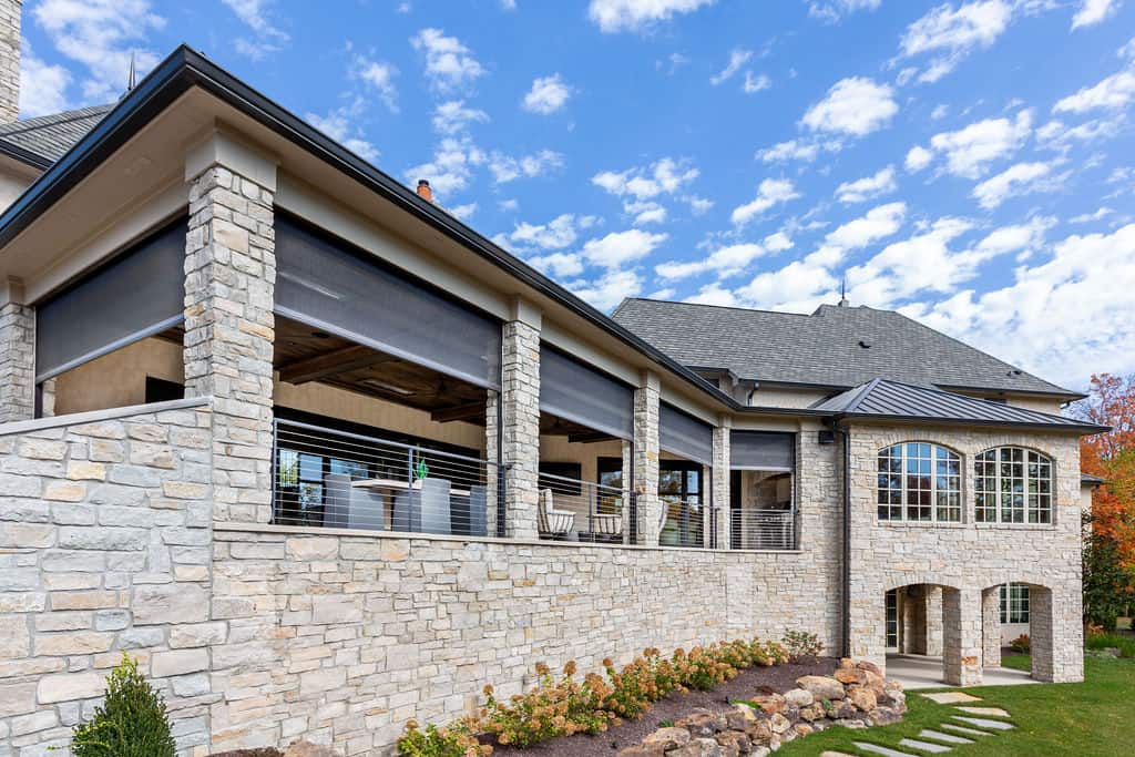 Nicholas Design Build | Modern stone house with a large covered patio, featuring arched windows and a manicured garden.