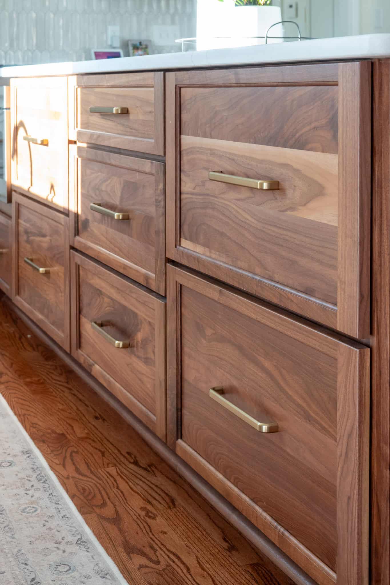 Nicholas Design Build | Wooden kitchen cabinets with brass handles and a white countertop on a hardwood floor.