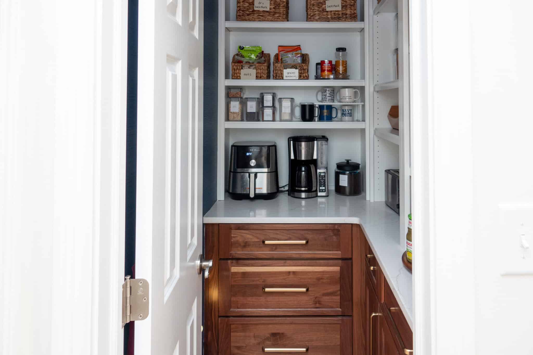 Nicholas Design Build | A pantry with wooden drawers, an air fryer, a coffee maker, and kitchen items on shelves.